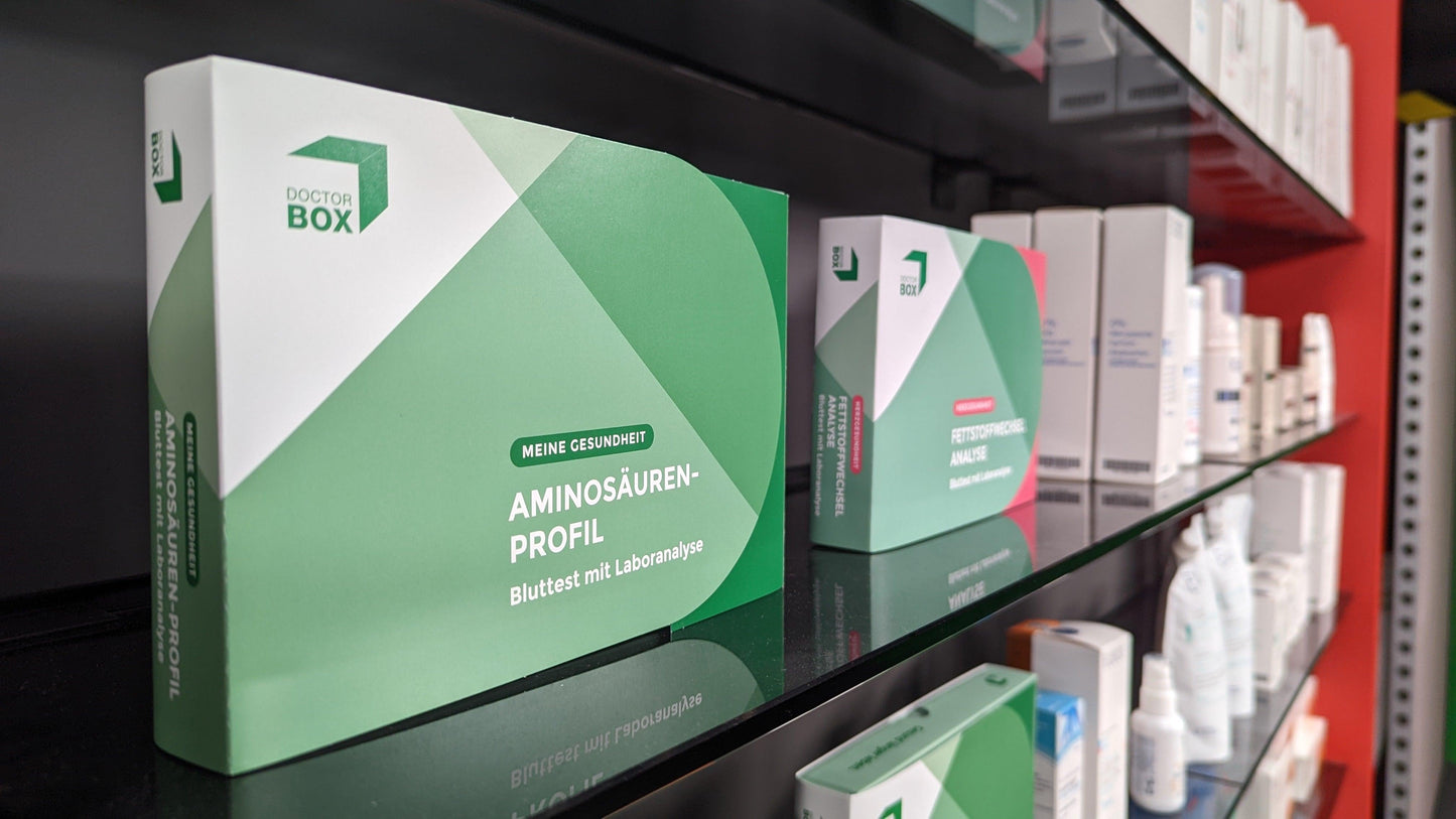 Die Verpackung des Aminosäuren Profils, das in einem Apothekenregal steht. Dahinter weitere Artikel der Apotheke.