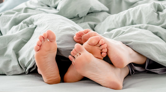 Zu erkennen sind die Füße eines Pärchens im Bett, die Fußsohlen sind sichtbar.