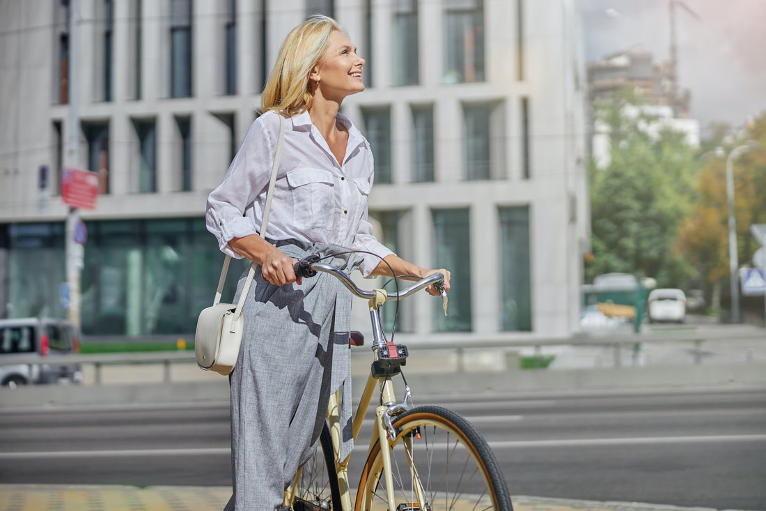 Glückliche und zufriedene Frau Ende 40, Anfang 50 steht mit ihrem Fahrrad und schaut nach oben, strahlt Ruhe und Ausgeglichenheit aus.